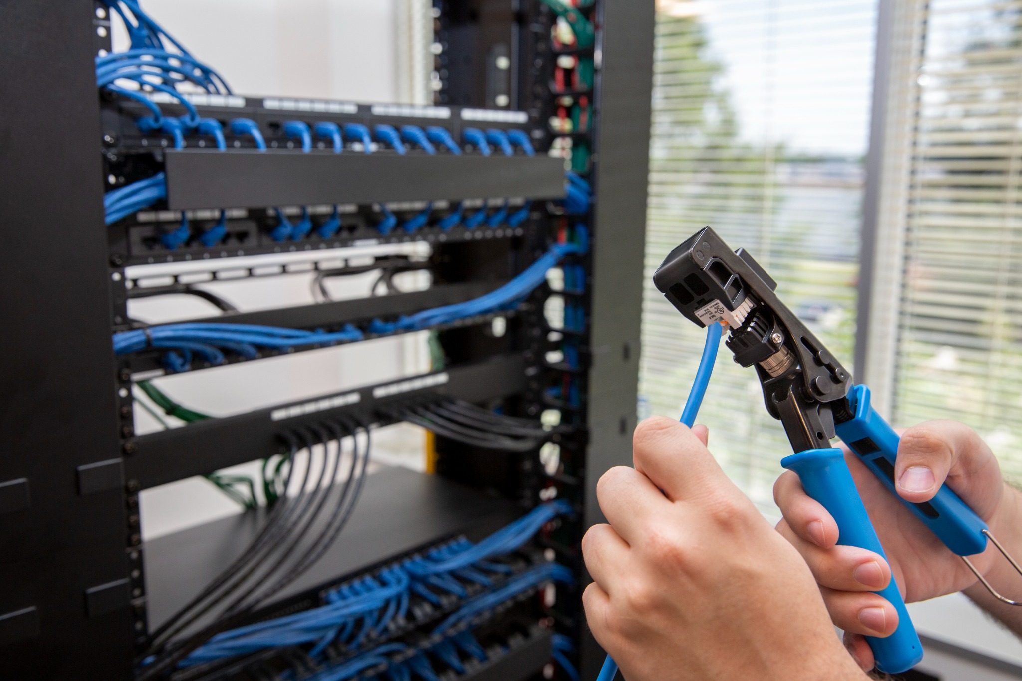 Technician terminating network cabling beside an equipment rack